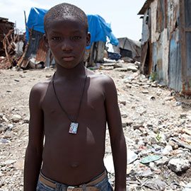 Ein Kind steht vor durch ein Erdbeben beschädigten Wellblechhütten in Haiti