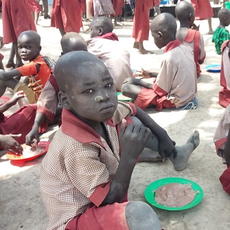 Eine Gruppe von der Krise in Süd-Sudan betroffener Kinder verspeist am Boden sitzend eine Mahlzeit
